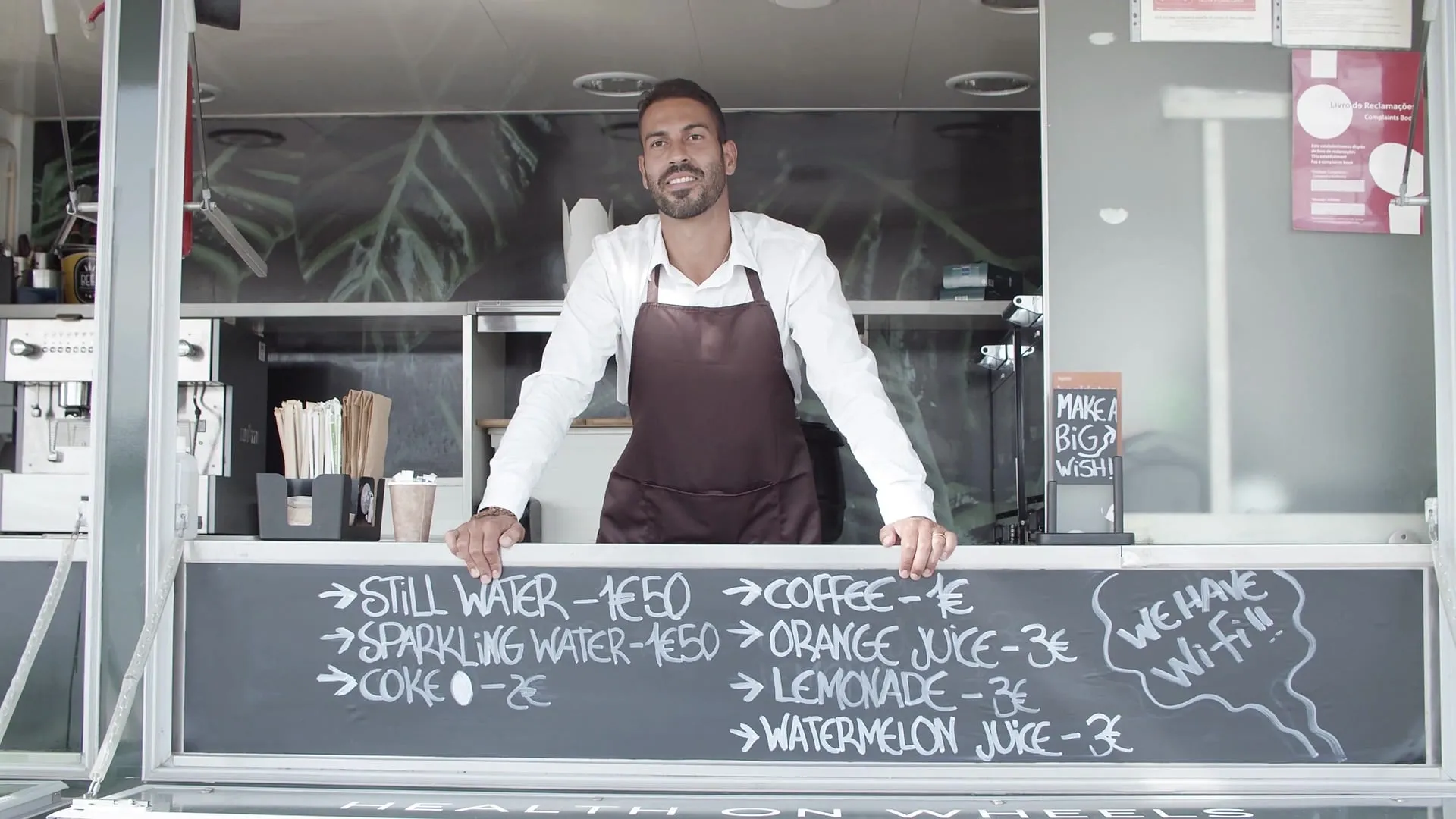 Coffee truck owner smiling and waving from behind his counter